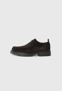 Zapato de ante marrón oscuro con cordones, suela gruesa negra y tirador, sobre fondo gris, vista lateral.