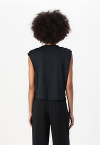Top corto negro sin mangas, hecho de una tela suave, con un escote redondo y un corte relajado, combinado con pantalones negros sueltos.