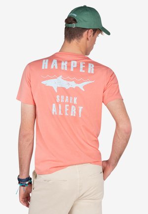 Camiseta de color coral con texto gráfico blanco "HARPER" y "ALERTA DE TIBURÓN" junto a una ilustración de un tiburón. Confeccionada en suave tela de algodón, con diseño de cuello redondo.