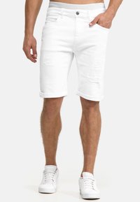 Witte denim shorts met distressed details, opgerolde broekspijpen, vijf zakken en een gebrandmerkt tailleband. Gecombineerd met witte sneakers.