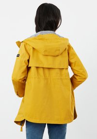 Żółta wodoodporna kurtka z kapturem, z szarą podszewką w paski, elastycznym pasem i bocznymi kieszeniami. Otwór z tyłu.