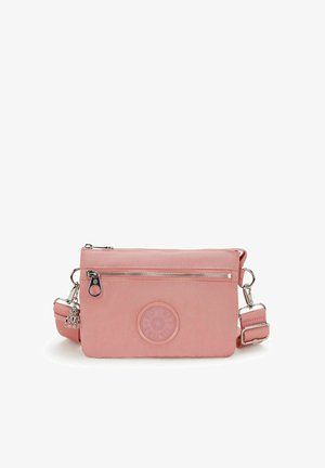 Malá růžová crossbody taška s přední kapsou na zip, nastavitelným popruhem, kulatou nášivkou s logem a malým stříbrným přívěskem ve tvaru opičky.