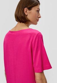 Rosa Kurzarmoberteil mit Rundhalsausschnitt, das eine glatte Textur und minimale Nahtdetails am Saum und am Ausschnitt aufweist.