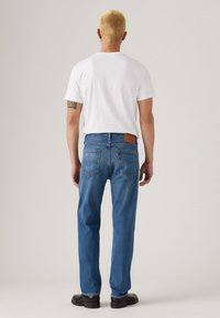 Blauwe spijkerbroek met een recht model, tan leren patch en achterzakken. Gecombineerd met een effen witte t-shirt met korte mouwen.