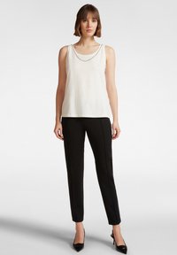 Witte mouwloze top met een lichte glans en ronde halslijn, gecombineerd met zwarte slim-fit broek en puntige zwarte hakken.