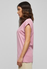 Light pink short-sleeve t-shirt made of soft fabric. It features a relaxed fit and minimal stitching details, displayed on a model from the side.