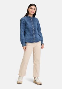 Jeansowa kurtka z kołnierzykiem, zapięciem na guziki i długimi rękawami. W zestawie z beżowymi spodami typu cropped i beżowymi trampkami.