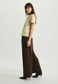 T-shirt en coton beige à manches courtes et col rond, associé à un pantalon large marron et des escarpins noirs à bout pointu.