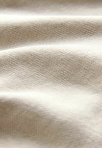 Tejido de color beige tejido con una textura suave, que presenta un sutil patrón diagonal y un ligero brillo gracias a hilos finos y suaves.