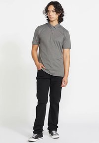 Szara koszulka polo z krótkim rękawem i kołnierzykiem, wykonana z gładkiej tkaniny. Połączona z czarnymi spodniami o wąskim kroju oraz czarnymi trampkami.