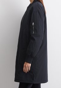 Czarna kurtka bombowa z zamkiem błyskawicznym na rękawie, ściągaczami przy mankietach i matowym wykończeniem. Posiada luźny krój oraz kieszenie boczne.