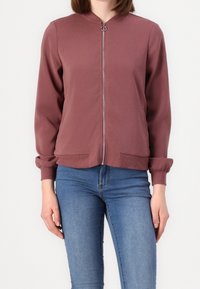 Mörk röd zip-up jacka med rund krage, ribbade ärmar och sidofickor; tillverkad av slätt tyg med en något avslappnad passform.