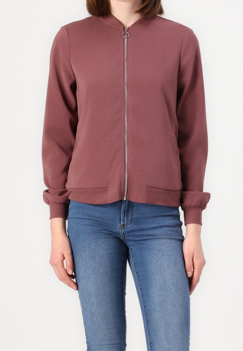 Mörk röd zip-up jacka med rund krage, ribbade ärmar och sidofickor; tillverkad av slätt tyg med en något avslappnad passform.