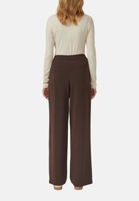 Braune, weit geschnittene Hosen mit einem elastischen Bund und zwei Gesäßtaschen, kombiniert mit einem eng anliegenden, hellfarbenen Langarmshirt.