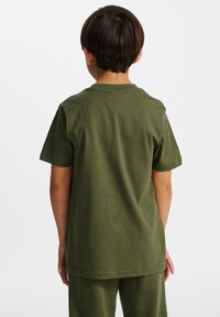 Zielona koszulka bawełniana z krótkim rękawem, okrągłym dekoltem i standardowym krojem, widoczna z tyłu. Brak widocznych wzorów lub grafik.