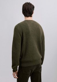 Maglione verde a coste con scollo rotondo e vestibilità morbida, realizzato in tessuto testurizzato; indossato con pantaloni scuri.