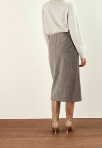 Jupe crayon grise à carreaux avec une taille haute, complétée par des bottes beiges à talons montant jusqu'aux genoux et un pull texturé gris clair.