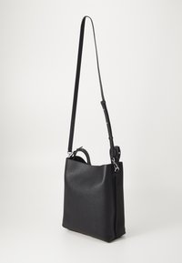 Sac à épaule en cuir noir avec une texture granuleuse, de forme rectangulaire, bandoulière réglable et anse supérieure. Caractéristiques de ferrures en argent.