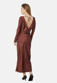 Ruda satino suknelė su ilgomis rankovėmis, giliu iškirpimu nugaroje ir drapiruotu dizainu. Yra kaklo juostos užsegimas ir siekia kulkšnis.