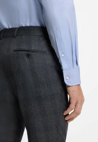  Lichtblauw overhemd met knoopmanchetten, gecombineerd met donkergrijze geblokte broek met een knoop achterzak. Zachte, gestructureerde materialen.