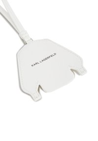 Biały skórzany identyfikator bagażu o unikalnym kształcie z wyciętym wzorem, wytłoczone logo "KARL LAGERFELD" oraz odczepiany pasek.