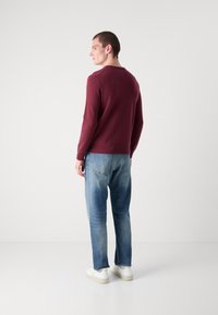 Pulover burgundy din material tricotat, cu guler rotund și mâneci lungi, asortat cu blugi ușor decolorați, de culoare albastru deschis, și adidași albi.