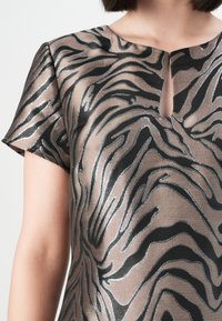 Kjole med korte ermer i bronse med teksturert zebra-print i svart og sølv. Har en nøkkelhullsutskjæring foran.