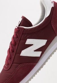 Baskets bordeaux avec une tige en tissu texturé, un logo blanc en accent et une semelle en caoutchouc grise. Comprend une fermeture à lacets et un col rembourré.