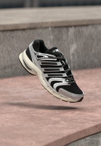 Schwarzer und silberner Sportschuh mit Mesh-Obermaterial, schlankem Design, reflektierenden Akzenten und weißer Sohle, schwebend vor neutralem Hintergrund.