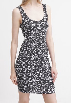 Robe sans manches à motif géométrique noir et blanc, longueur genou, ajustée, portée par une personne debout avec les bras détendus le long du corps.