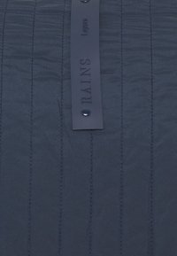 Dzianina w kolorze granatowym ze wzorem pikowania, z pionowymi szwami. Ma matową czarną metkę z wytłoczonym napisem oraz czarny zamek zatrzaskowy.