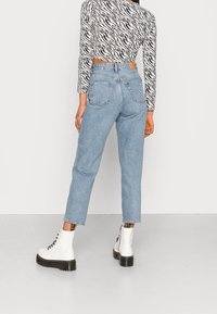 Lichtblauwe spijkerbroek met hoge taille, rechte pijpen en twee achterzakken. Gepaard met witte veterschoenen. Zwart-wit gestippeld shirt zichtbaar.