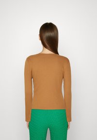 Ruskea poimullinen pitkähihainen paita, jossa on pyöreä pääntie, yhdistettynä teksturoiduihin vihreisiin housuihin. Kangas näyttää pehmeältä ja sovitetulta.