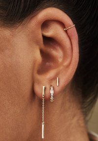 Boucles d'oreilles dorées avec un design à chaîne, barres rectangulaires et un anneau avec des pierres incrustées, mettant en valeur des textures métalliques polies.