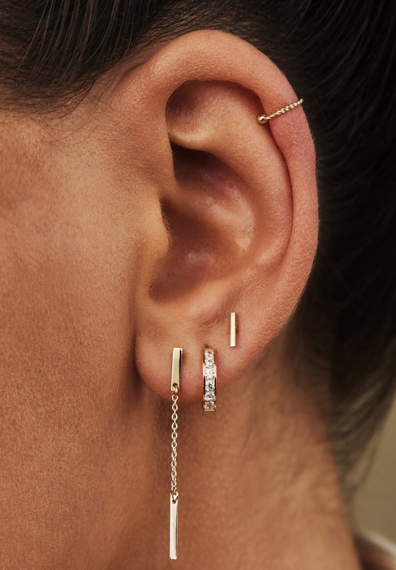 Boucles d'oreilles dorées avec un design à chaîne, barres rectangulaires et un anneau avec des pierres incrustées, mettant en valeur des textures métalliques polies.