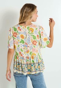 Blusa de estampado floral en crema con mangas cortas con volantes, un escote en forma de lágrima en la espalda y un dobladillo peplum que cuenta con un acento a rayas en la parte inferior.