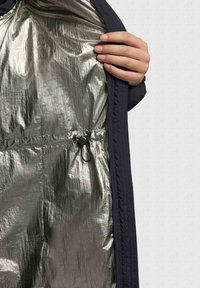 Gewatteerde jas met een donkere buitenzijde en een glanzende zilveren binnenkant. Voorzien van een trekkoord met een schuifje om de pasvorm aan te passen.