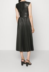 Robe en cuir noir avec un haut ajusté et une jupe plissée. Manches courtes et fermeture éclair au dos. Porte avec des sandales à talons noires.