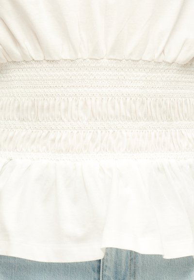 Λευκό ύφασμα με οριζόντιες ελαστικές πτυχώσεις και μαζερό τελείωμα βολάν πάνω από ανοιχτόχρωμο μπλε τζιν.