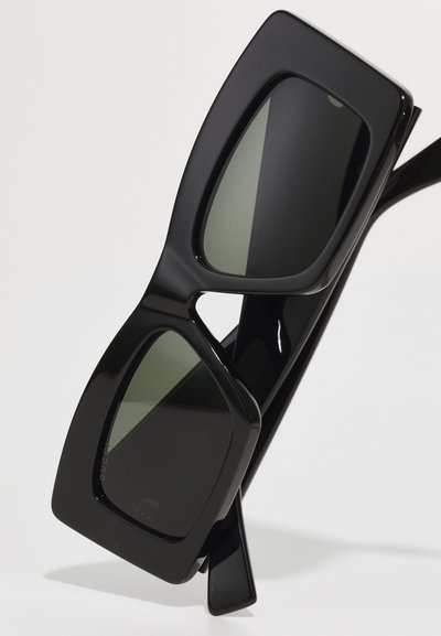 Ochelari de soare dreptunghiulari negri cu lentile verzi. Rame grosiere, textură netedă și design ușor unghiular. Fără logo-uri sau modele vizibile.