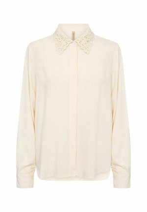 Blusa larga de color crema con mangas largas, cuello bordado de encaje, tapeta frontal con botones y puños plisados.