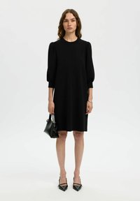 Musthave mustrippi lühikeste puhvärviliste varrukatega, ümmarguse kaelusega ja põlvepikkusega disain. Ühendatud terava musta kontsaga ja väikese musta käekotiga.