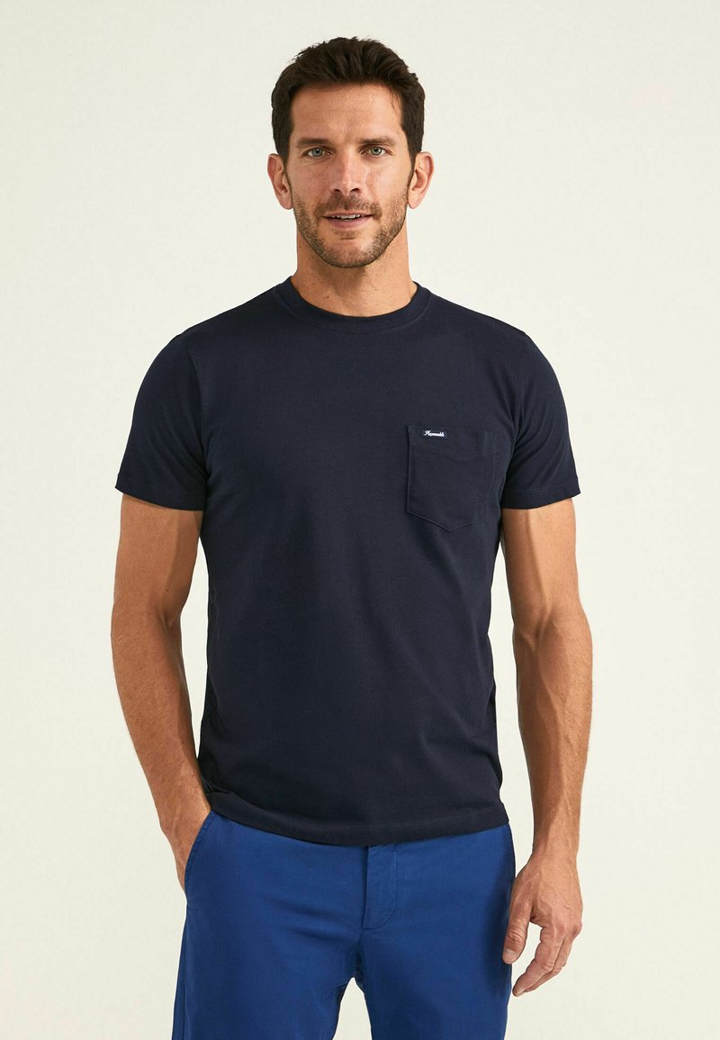 Camiseta de manga corta azul marino de algodón, con cuello redondo y un bolsillo en el pecho izquierdo con una pequeña etiqueta de la marca. Textura suave, corte casual.