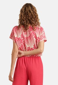 Short-sleeve crop top in pink with an abstract white leaf pattern, paired with textured pink pants. Relaxed fit with a round neckline.