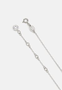 Srebrn ton ogrlica s prozornim kristalnim obeskom. Ima fine verige in okroglo sponko, ki prikazuje preproste geometrijske povezave.