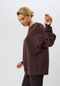 Sudadera marrón de gran tamaño con puños y dobladillo acanalados, que presenta una textura suave y un corte relajado. Se combina con leggins de estampado de leopardo negro.