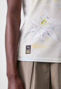 Débardeur de couleur claire, texturé, avec un motif floral blanc et un logo "Puma" noir accompagné du texte "AUTHENTIC LICENSED FOOTBALL".