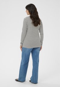 Cămașă cu mâneci lungi, crem, cu dungi orizontale negre, asortată cu blugi albaștri cu croială lejeră și pantofi negri, văzută din spate.