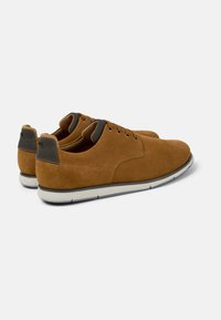 Pantofi din suede maro cu o textură netedă, vârf rotund și accente din material gri la călcâi și limbă. Talpă din cauciuc albă cu margine neagră.