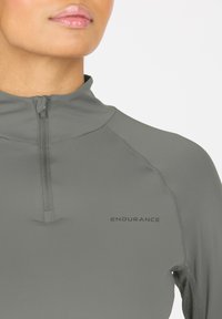 Grå atletisk langærmet top med lynlås krave, der har en glat tekstur og trykt "ENDURANCE" logo på brystet.